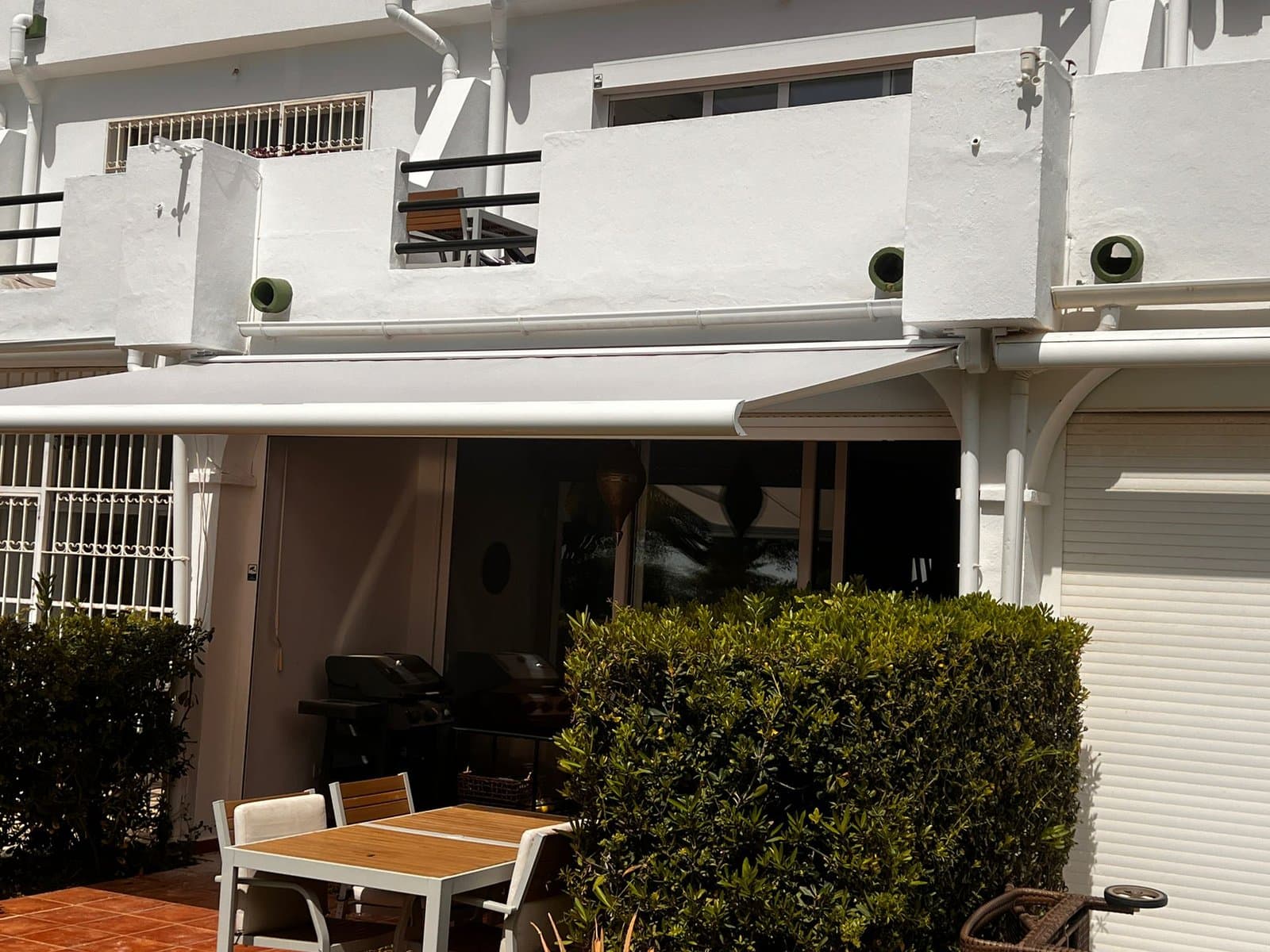 Cream retractable arm awning over a white townhouse terrace with a garden table