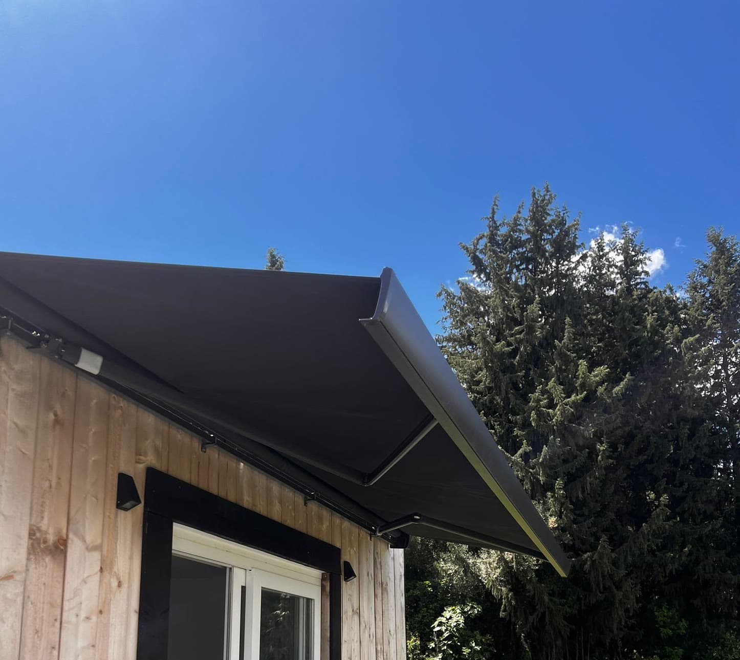 Charcoal cassette awning extended from a timber-clad garden room against a blue sky